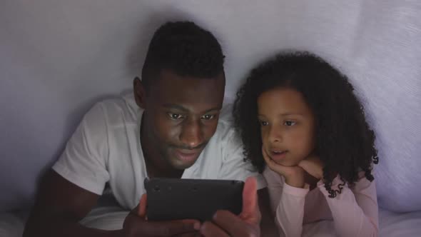 African american father and daughter looking at phone in bed alt