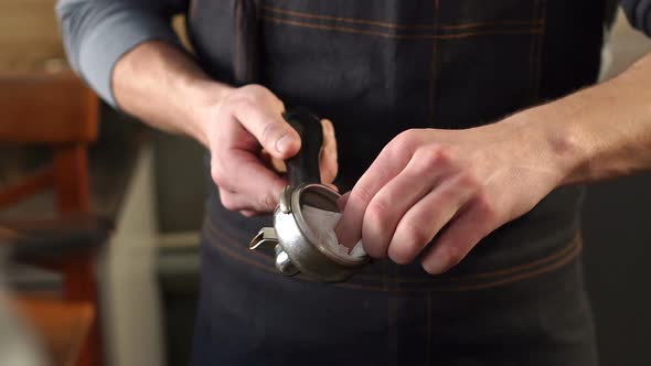 Closeup of a Male Barista Wipes a Portafilter for Ground Coffee with a Napkin alt