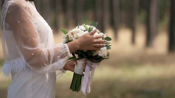A bride in a white dress adjusts and sniffs a wedding bouquet of roses