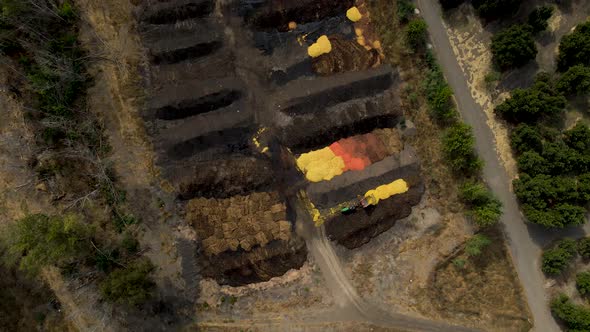 Aerial top down dolly in of a tractor discarding orange shells in a compost area surrounded by plant alt