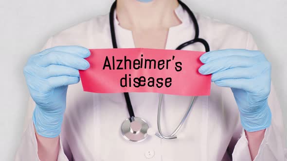 Closeup, Hands in Blue Medical Gloves Hold and Tear Red Paper Card with an Inscription Alzheimer's alt