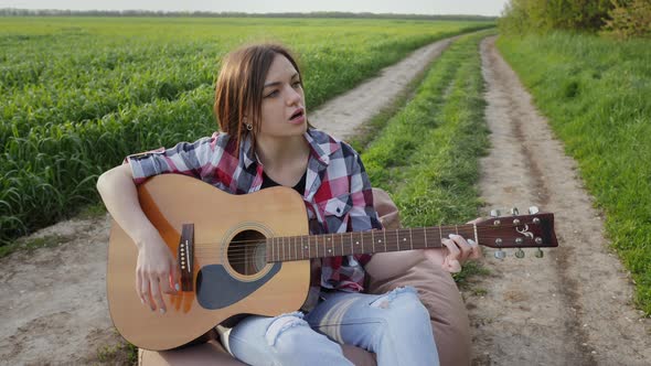 Woman Plays Music on Guitar and Sings on the Country Road Near Wheat Field