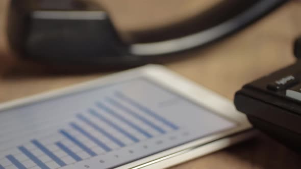 Office phone and tablet with blue bar chart displayed on screen alt