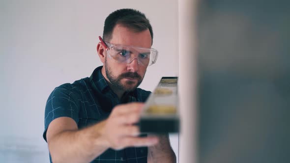 Handyman in Goggle Checks Wall Level at Room Renewal alt
