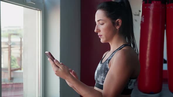 Female Martial Arts Masterusing Smart Phone with Personal Trainer Workout App in Gym alt