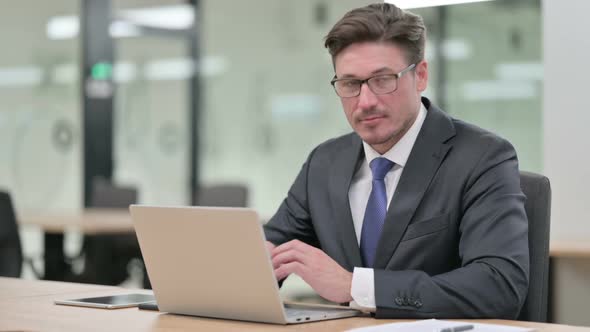 Middle Aged Businessman with Laptop Smiling at Camera in Office alt