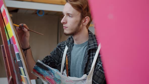 Portrait of Talented Young Man Arts Student Painting Picture in Studio Indoors alt