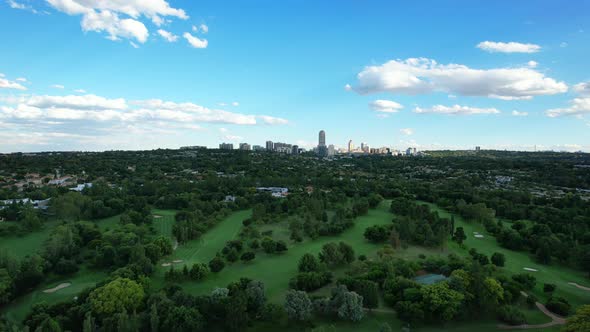green golf course with skyline of Sandton in Johannesburg during day, aerial alt