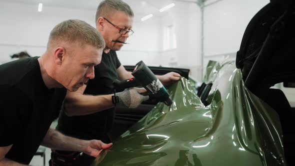 Men are Vinyl Wrapping a Car in Dark Green Color Using Heat Gun