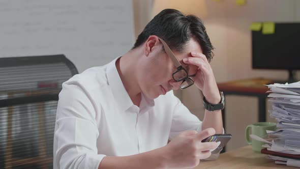 Close Up Of Asian Man Being Upset Losing Game On Smartphone After Working With Documents alt
