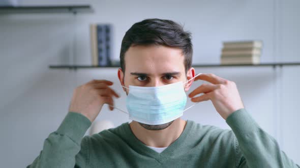 A young man puts on a blue medical mask. Young guy putting on a mask alt
