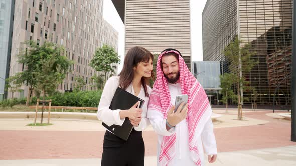 Cheerful Arab Man Showing Cellphone to Businesswoman alt