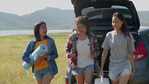 A group of young teen Asian women helps to hold backpacks and ice coolers with friends camping.