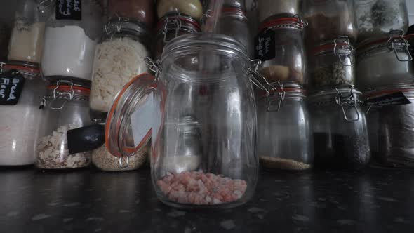 Himalayan rose pink salt pouring into Kilner clip top jar infant of wall of ingredients. alt
