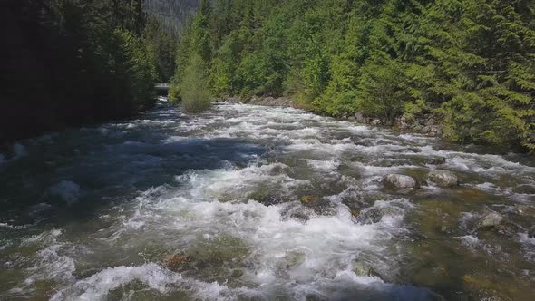 Aerial Drone Traveling Along Water Rapids With Mountains And Evergreen Forest 1