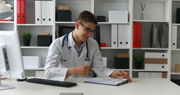 Young Doctor Researching Documents and Smiling at Camera