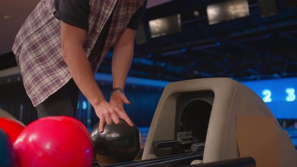 A Man in a Bowling Club Picks Up a Black Bowling Ball with the Number 8 in Slow Motion alt