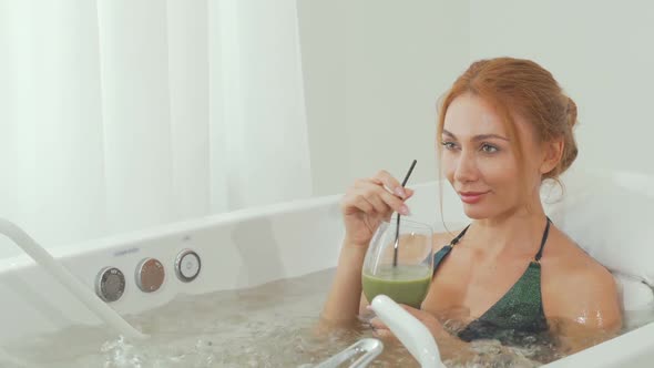 Sliding Shot of a Beautiful Woman Sipping Delicious Smoothie in Whirl Pool Bath