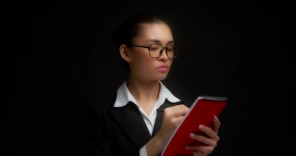 Business Woman Does Not Like What is Written in a Red Notebook alt