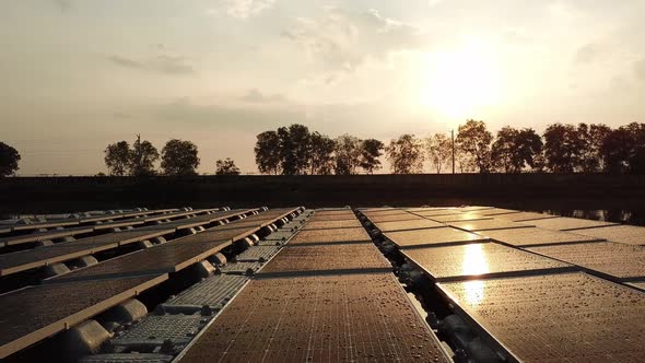 Aerial backwards flight showing solar panels reflection from sun during golden sunset alt