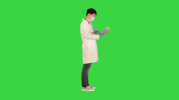 Young Asian Doctor is Working on Laptop Searching and Typing on a Green Screen Chroma Key alt