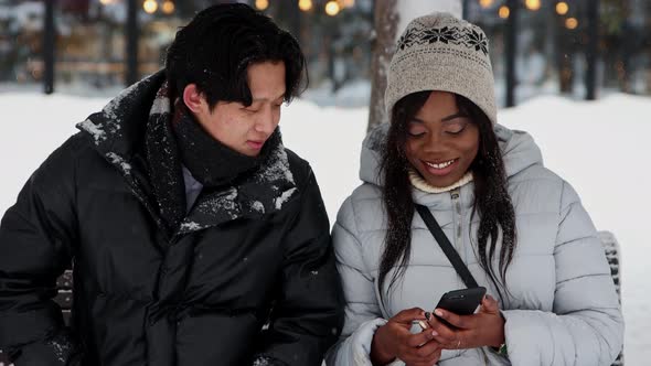 Young Black Woman Showing Pictures on Her Phone to Her Asian Boyfriend alt