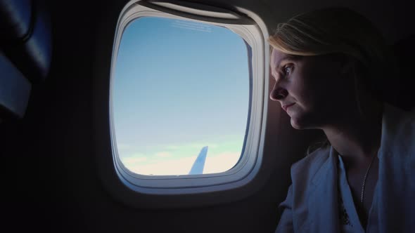 Lonely Sad Woman Looks Out the Porthole of the Plane alt