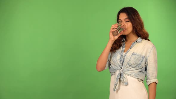 A Young Caucasian Woman Drinks a Glass of Water and Smiles at the Camera  Green Screen Background