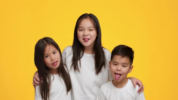 Cheerful Japanese Siblings Having Fun Grimacing Showing Tongues Yellow Background alt