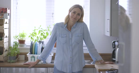 Serene woman standing in kitchen with arms crossed alt