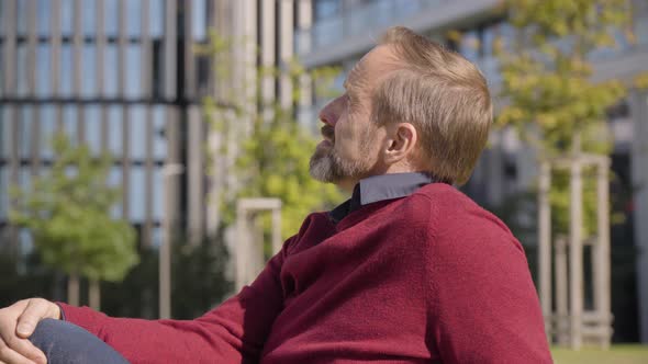 A Middleaged Handsome Caucasian Man Smiles at the Camera As He Sits in a Street in an Urban Area alt