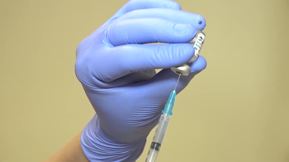 Unrecognizable Hands in Blue Medical Gloves Draw Vaccine From a Vial Into a Syringe