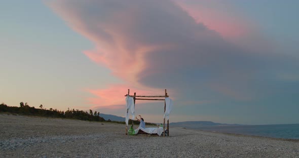 Young girl sleep on the gazebo bed during a insane sunset  on the beach alt