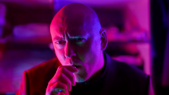 a Bald Gloomy Man Puffs on an Electronic Cigarette and Looks at the Camera in a Flashing alt
