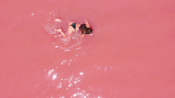 Aerial View of an Attractive Woman in a Bikini Floating in Pink Salt Lake alt