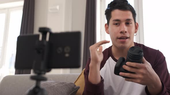 Young latin man talking on mobile camera, explaining a photo camera. Content creator concept alt