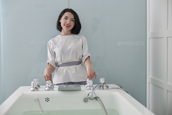 Portrait of woman assistant in uniform standing by contemporary hydro massage tub