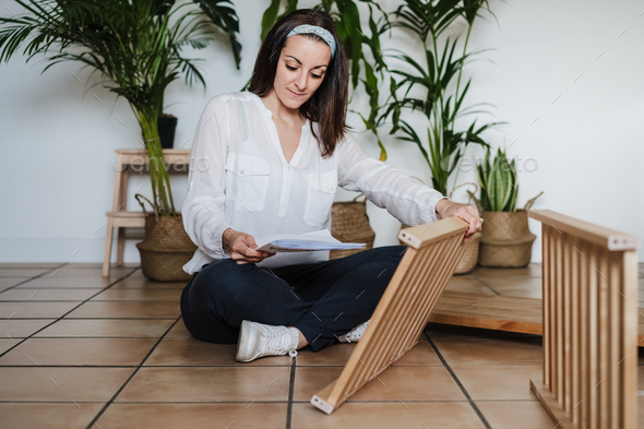 young woman assembling furniture at home reading instructions. DIY concept