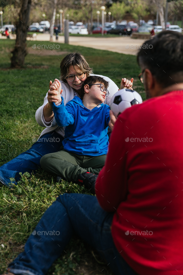 Boy with disability enjoys playing with a soccer ball with his parents outdoors in a park.