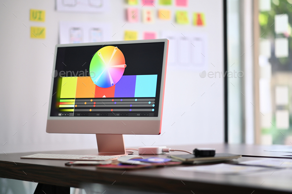 Graphic designer workplace with computer pc, stationery and color swatches on wooden table.