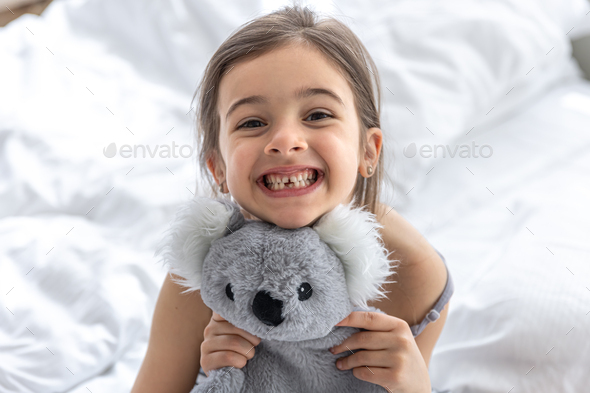 Happy little girl with soft toy koala in bed.