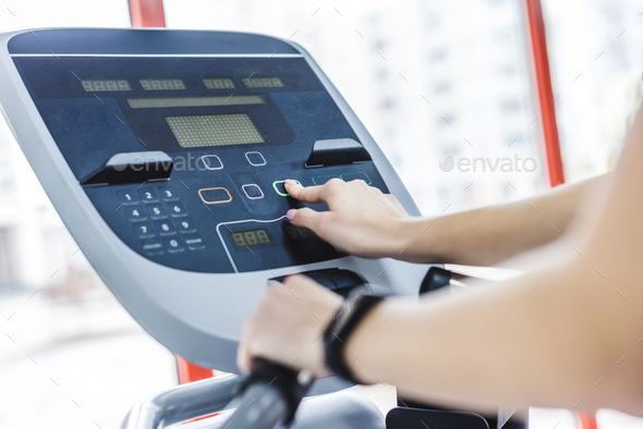 cropped shot of woman setting up elliptical machine at gym