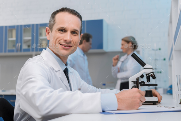 Smiling lab technician taking notes while doing microscope sample ...
