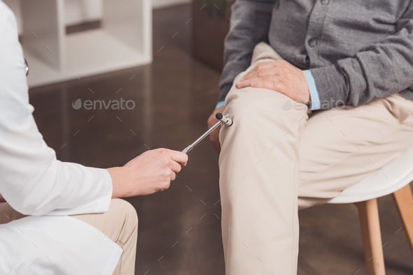 cropped shot of doctor examining patient with reflex hammer in clinic