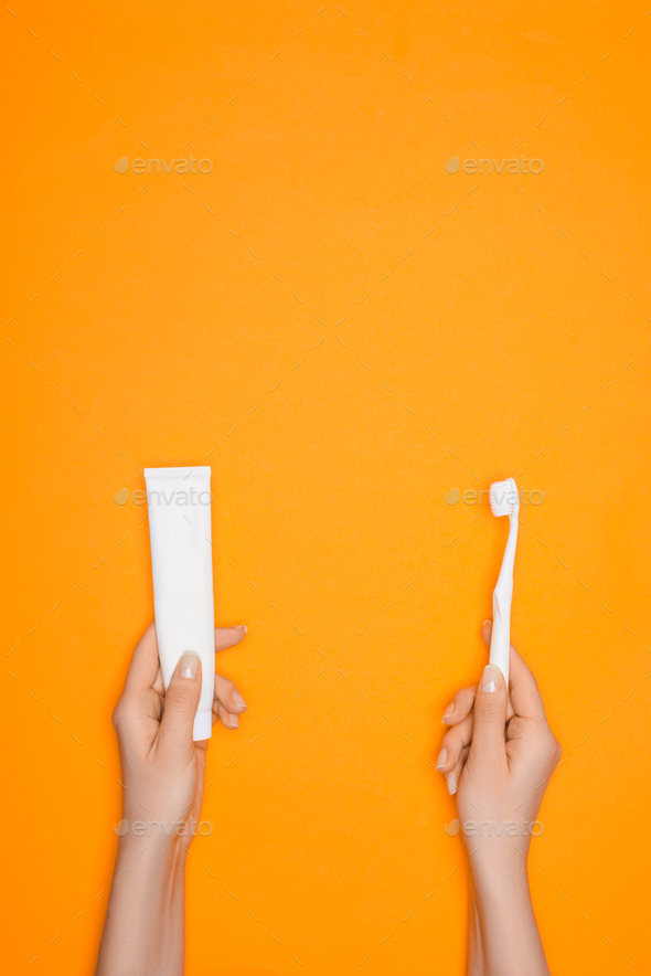 cropped view of woman holding toothbrush and tube of toothpaste, isolated on orange