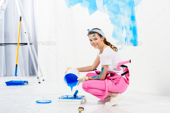 smiling girl pouring paint from bucket into plastic paint tray