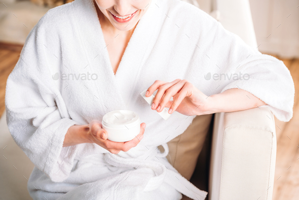 Cropped shot of woman in white bathrobe opening up a jar of face cream