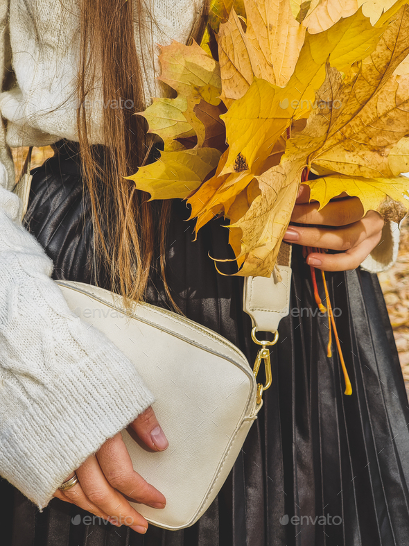 Closeup toned image of young stylish woman in sweater holding yellow autumn leaves in hands - Stock Photo - Images