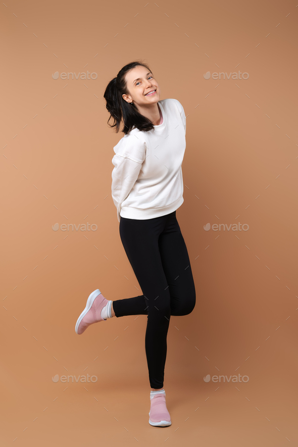 Sportive and playful girl in white pullover and black leggings grimace in studio