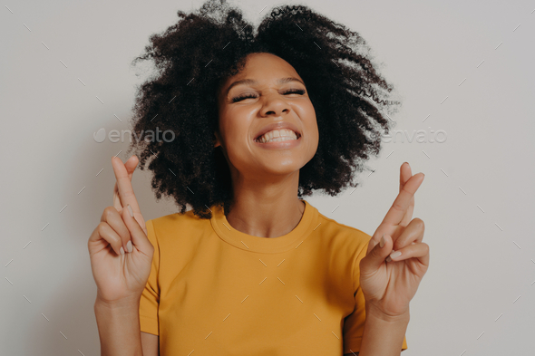 Head shot smiling beautiful African girl with closed eyes crossing fingers wishing good luck